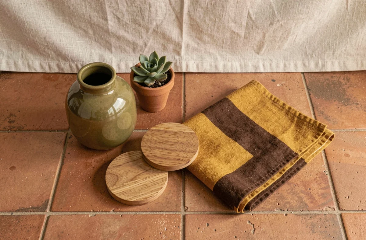 Flat-lay d'objets décoratifs style années 70 : vase céramique vert olive, textile rayé moutarde et chocolat, pot en argile brute