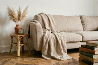 Jeté de canapé beige en lin texturé drapé sur un canapé arrondi dans un salon bohème chic avec parquet en chêne et décoration naturelle